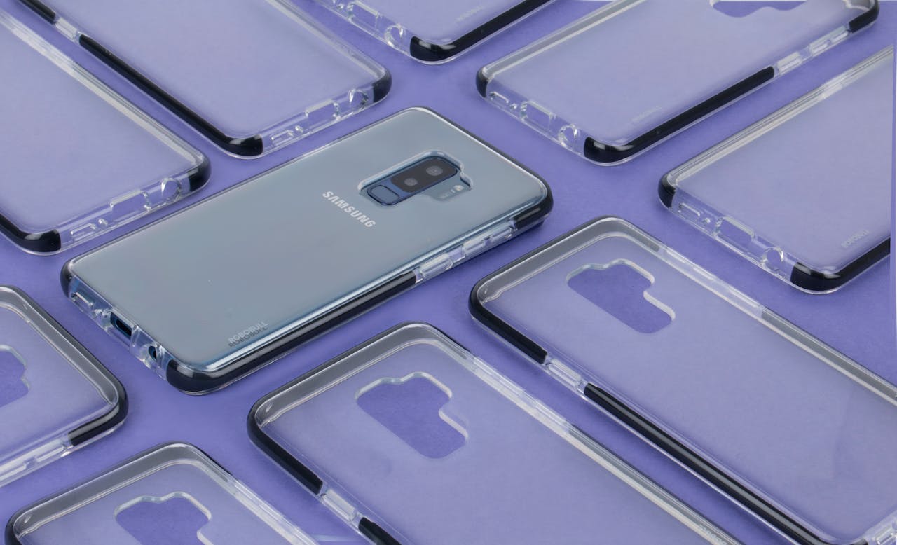 Close-up of a Samsung phone surrounded by transparent cases on a purple surface, showcasing modern technology.